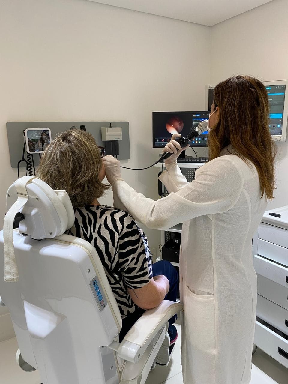 Dra. Viviane examinando o ouvido de uma paciente, com a imagem no monitor